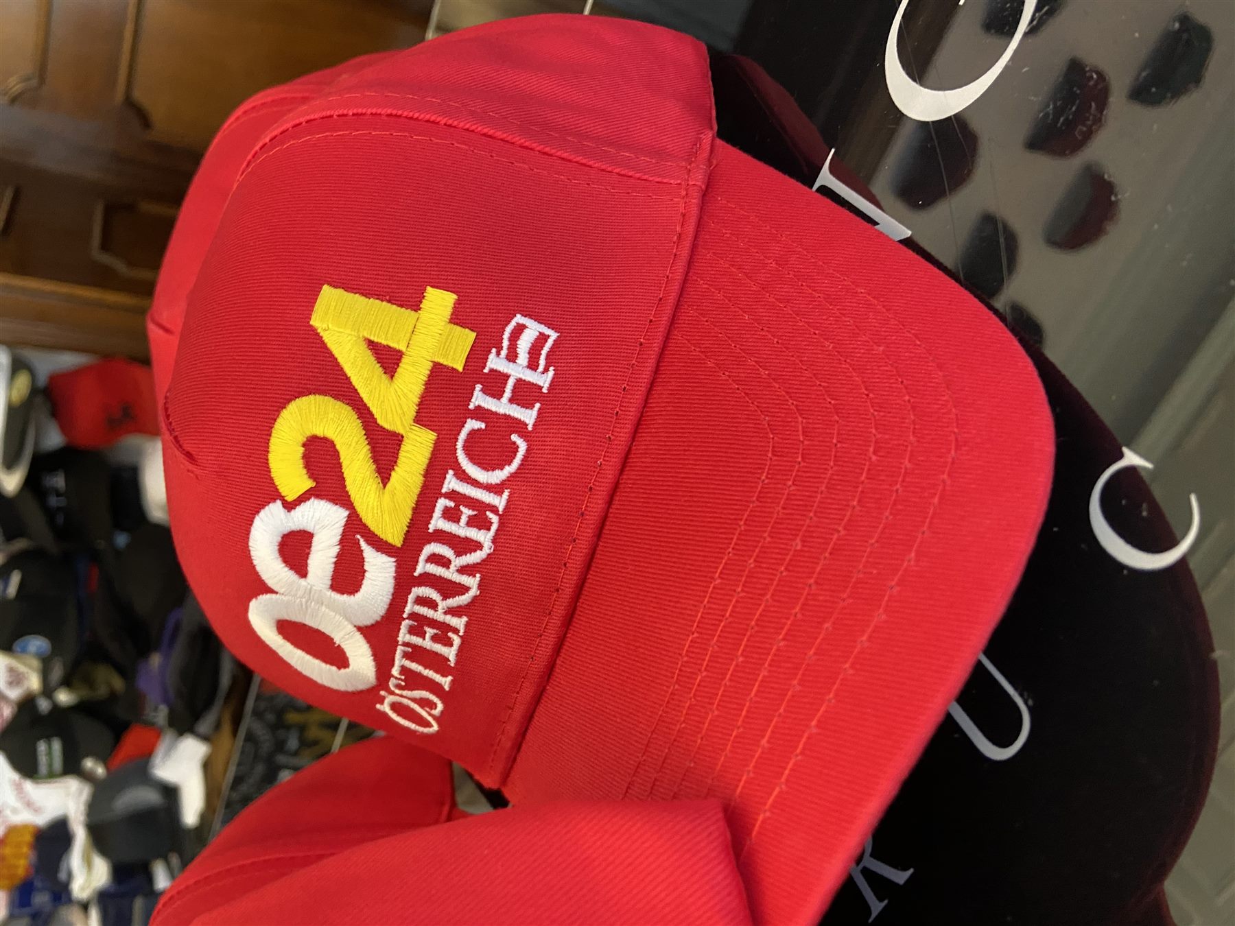 Red promotional caps hanging on a rack in the workshop, the front cap embroidered with a yellow and white logo.