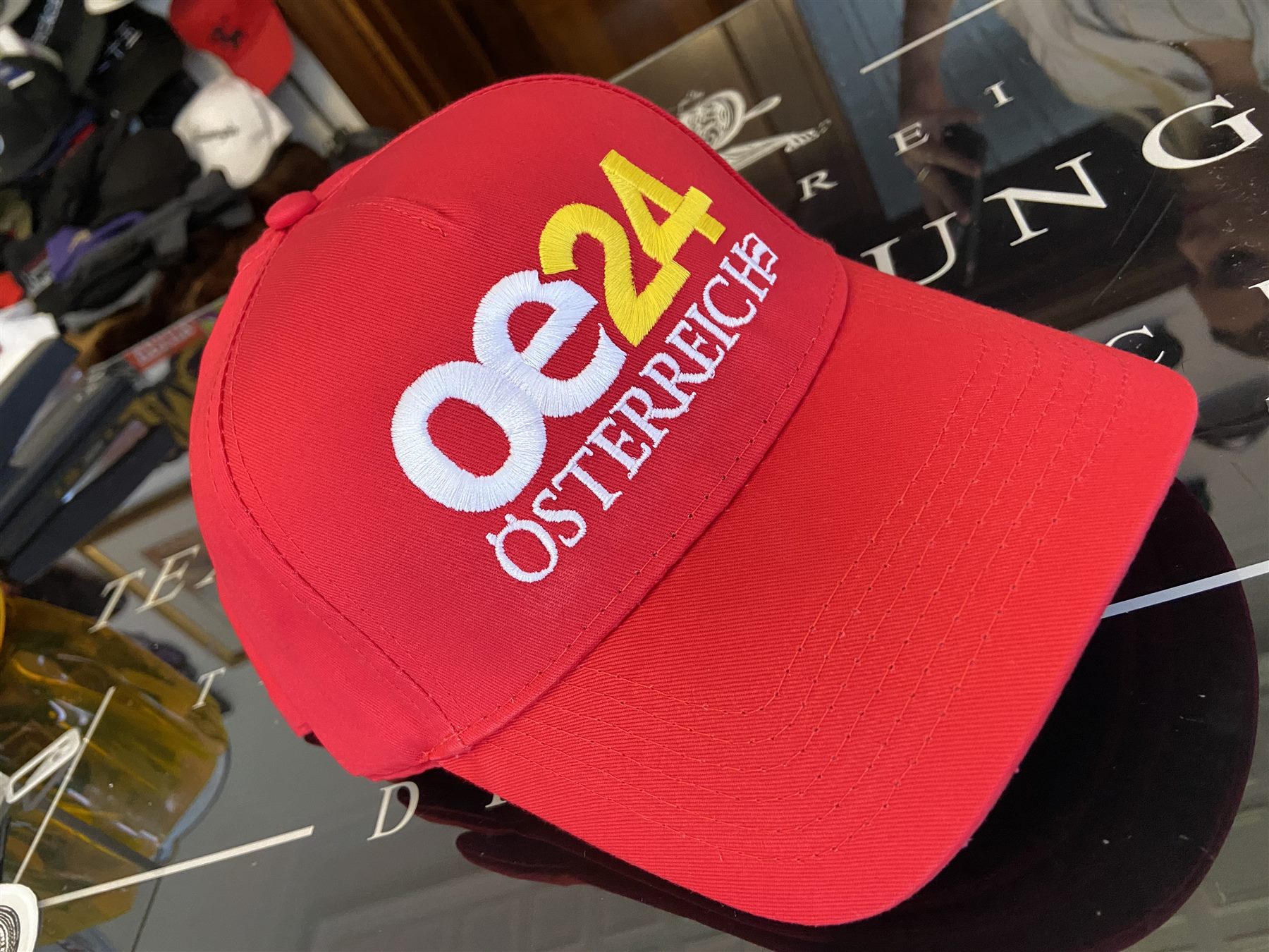 Red baseball cap with a white and yellow embroidered oe24 Österreich logo across the front panel.