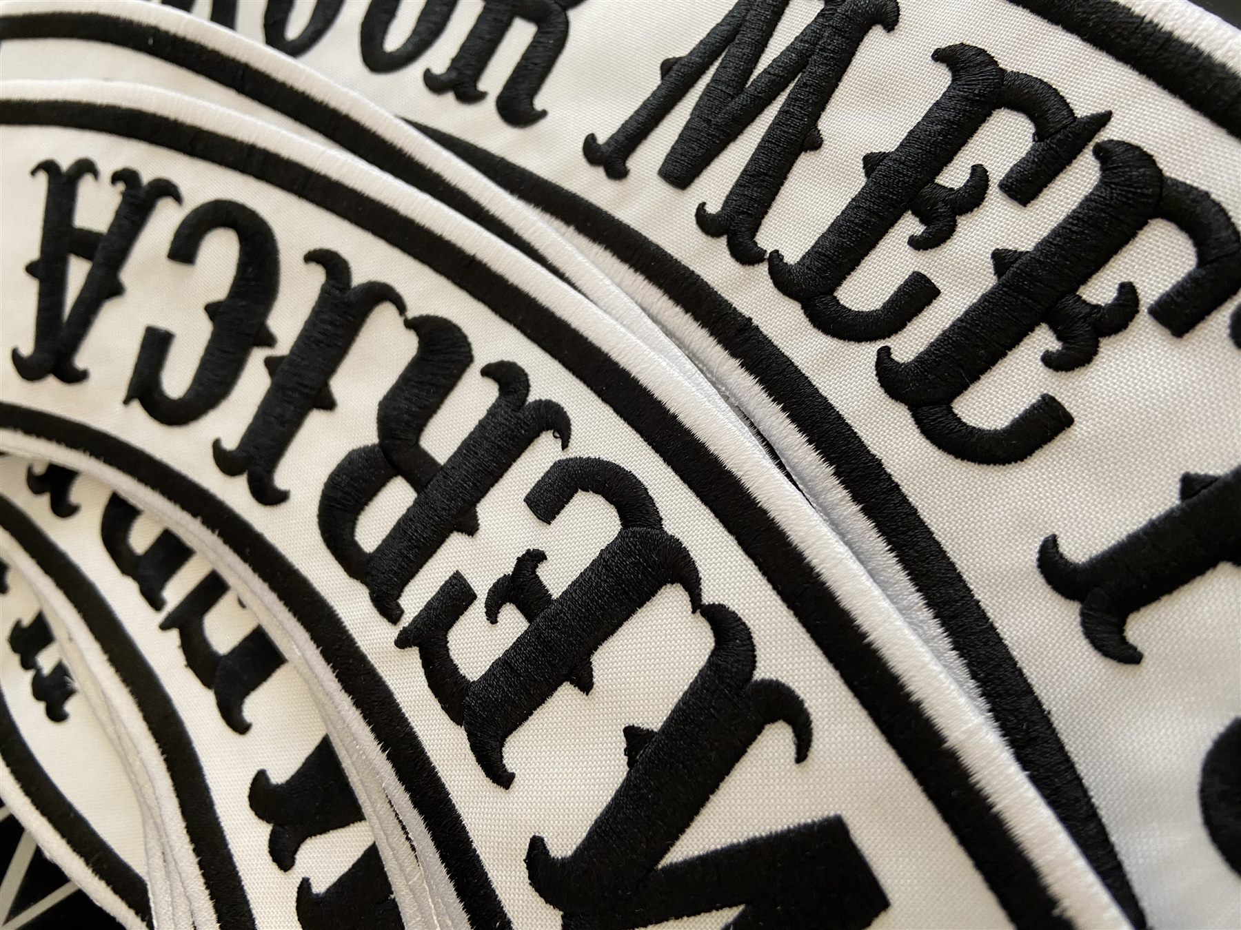 Close-up of large white embroidered patches with black lettering and a black border, stacked on top of each other.
