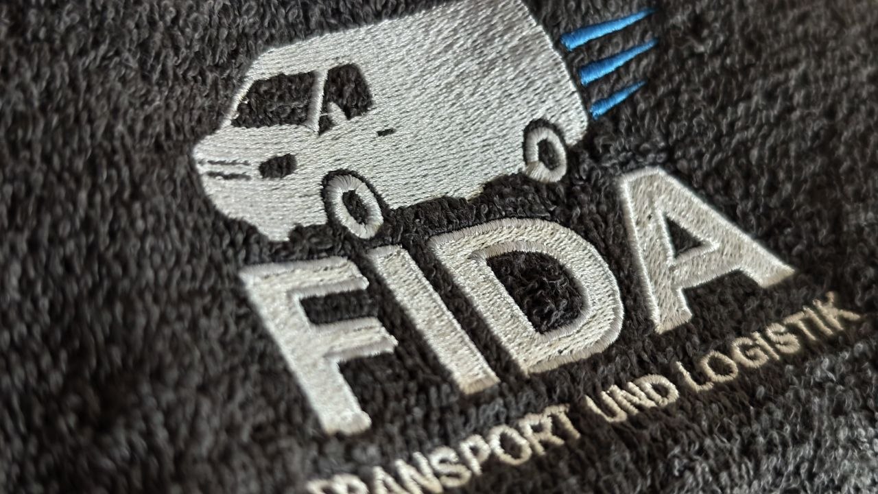 White transport company logo embroidered on dark textured fabric