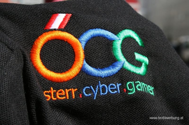 Close-up of a black pique polo shirt with a multi-colour embroidered logo in orange, blue and green above small embroidered lettering.